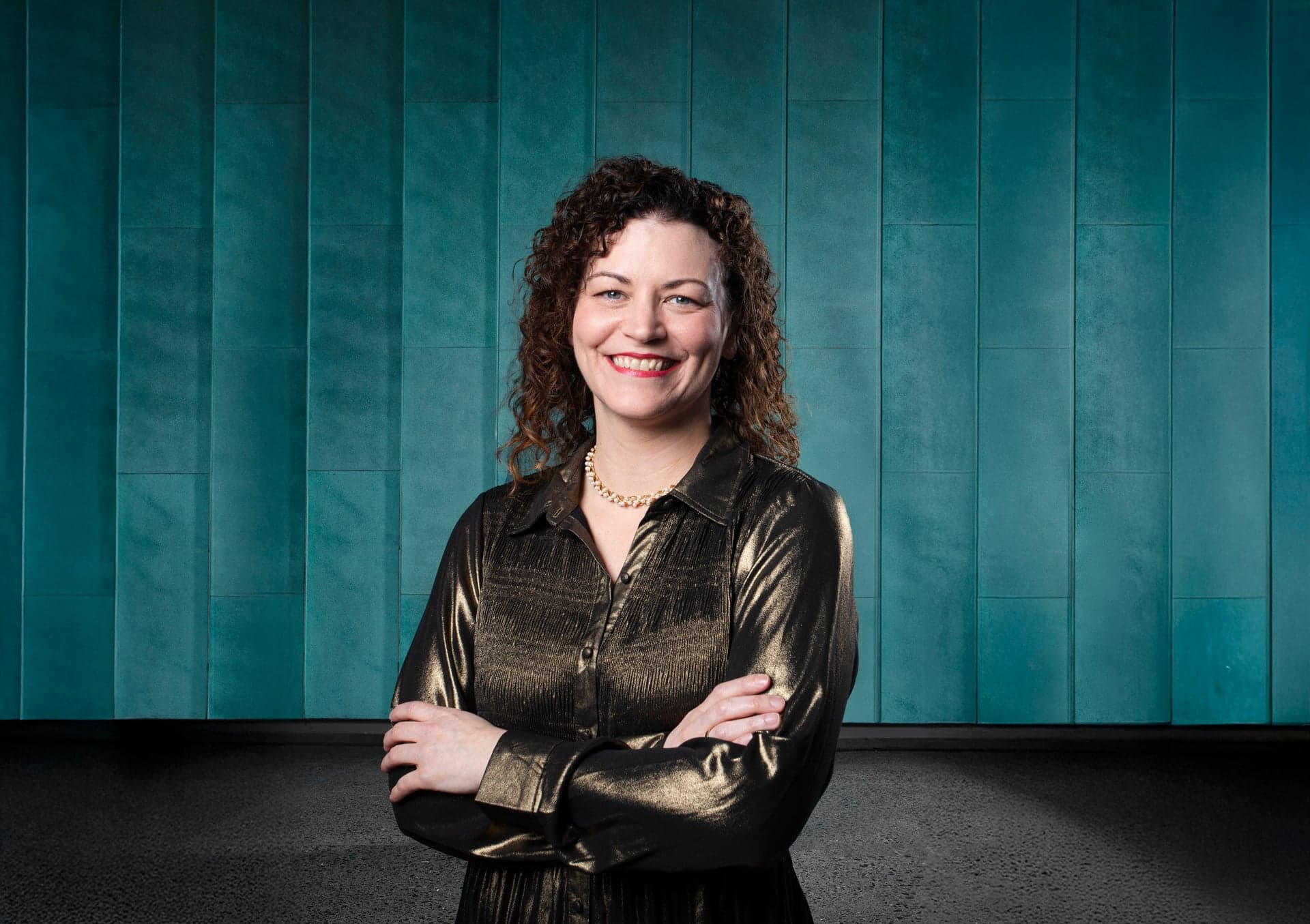 Katie Buckley with her arms folded, in front of a teal wall.