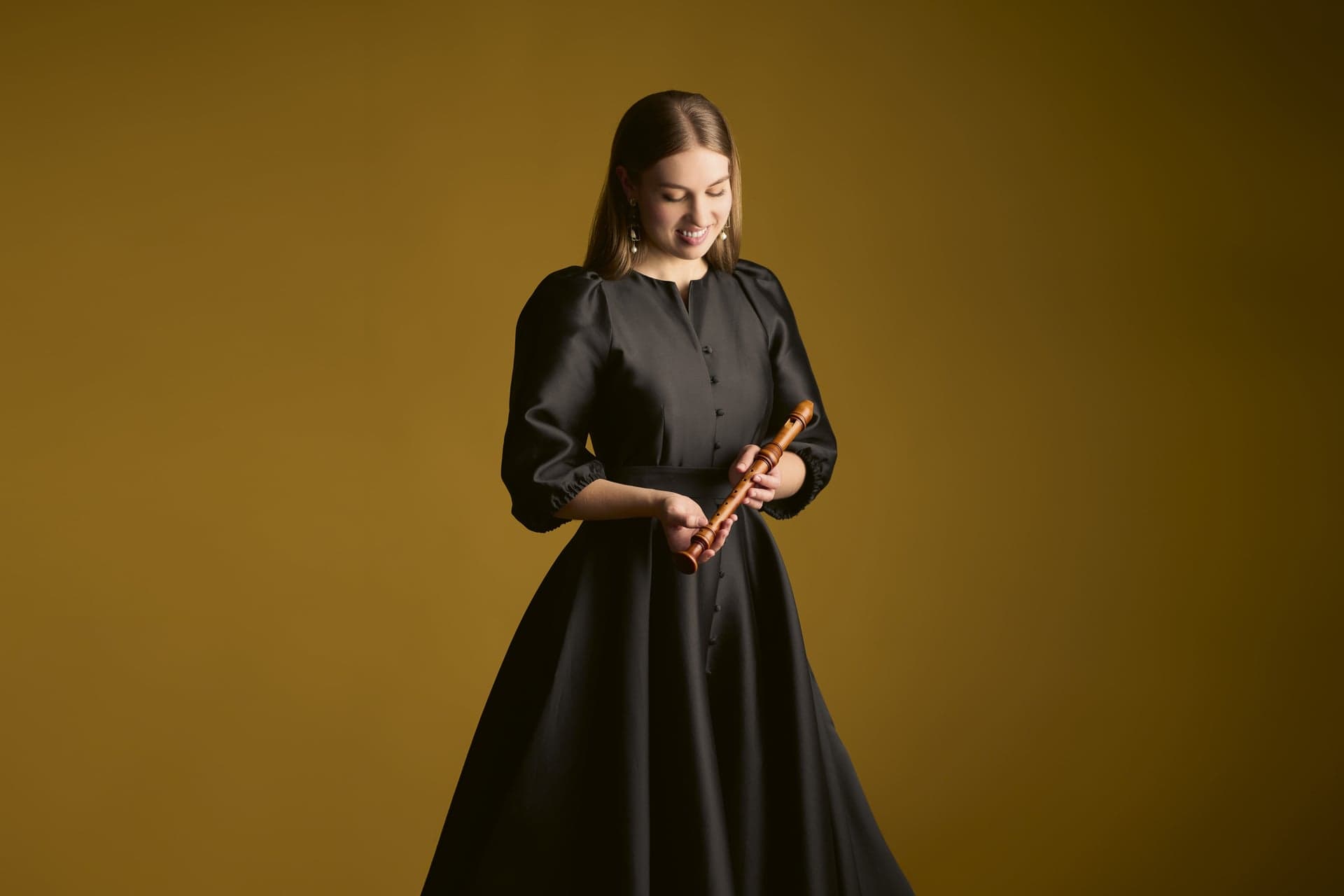 Lucie Horsch holds a recorder and looks down, against an olive-gold background.