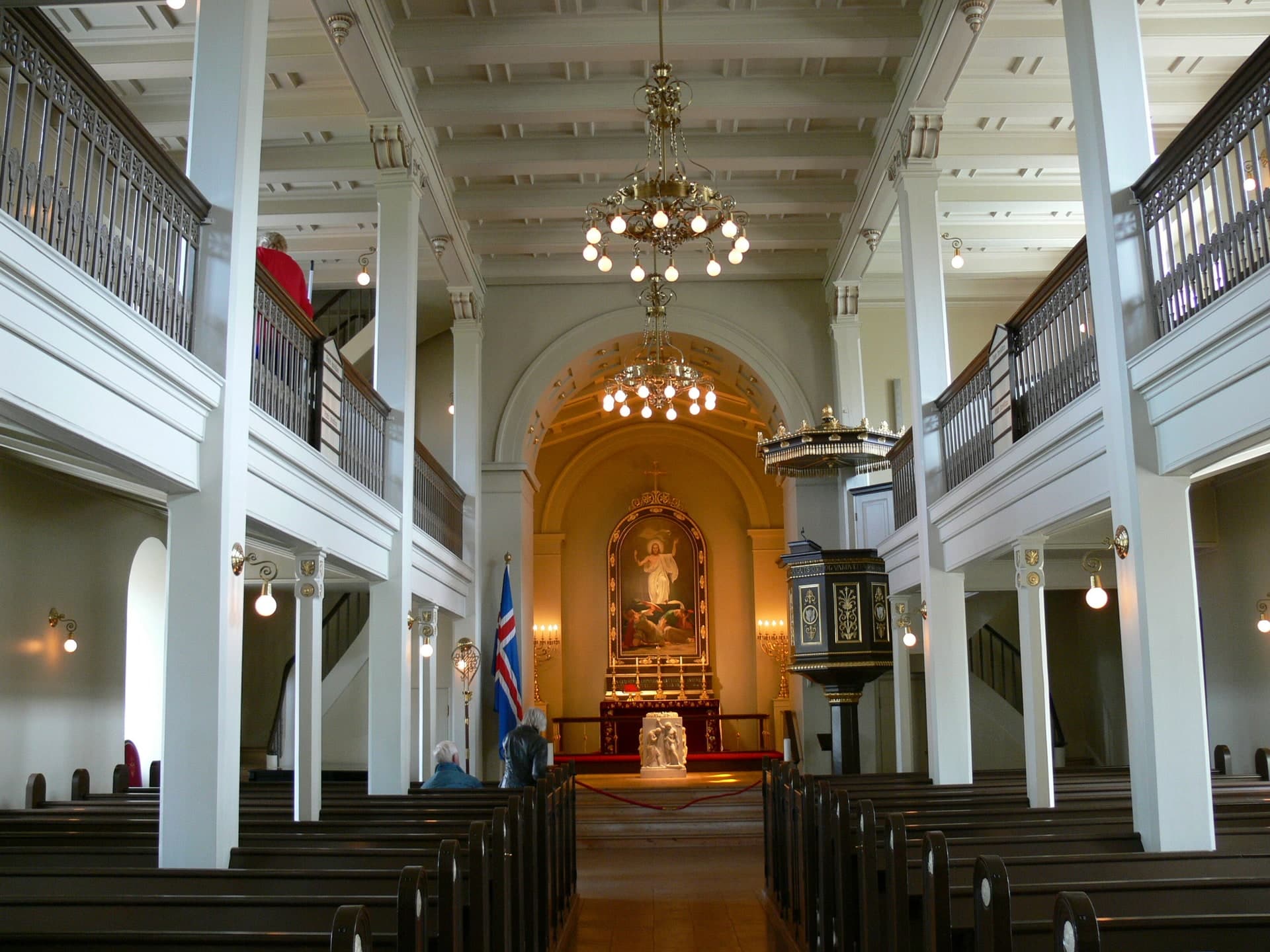 The nave of Dómkirkjan with dark pews, white columns and a gallery down either side, the altarpiece lit at the far end.