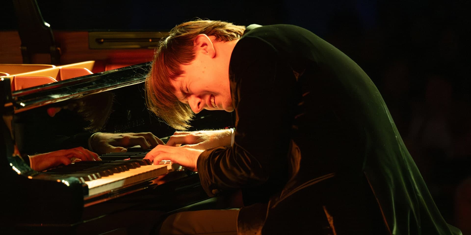 Grzegorz Niemczuk bent low over the keyboard of a grand piano on stage.