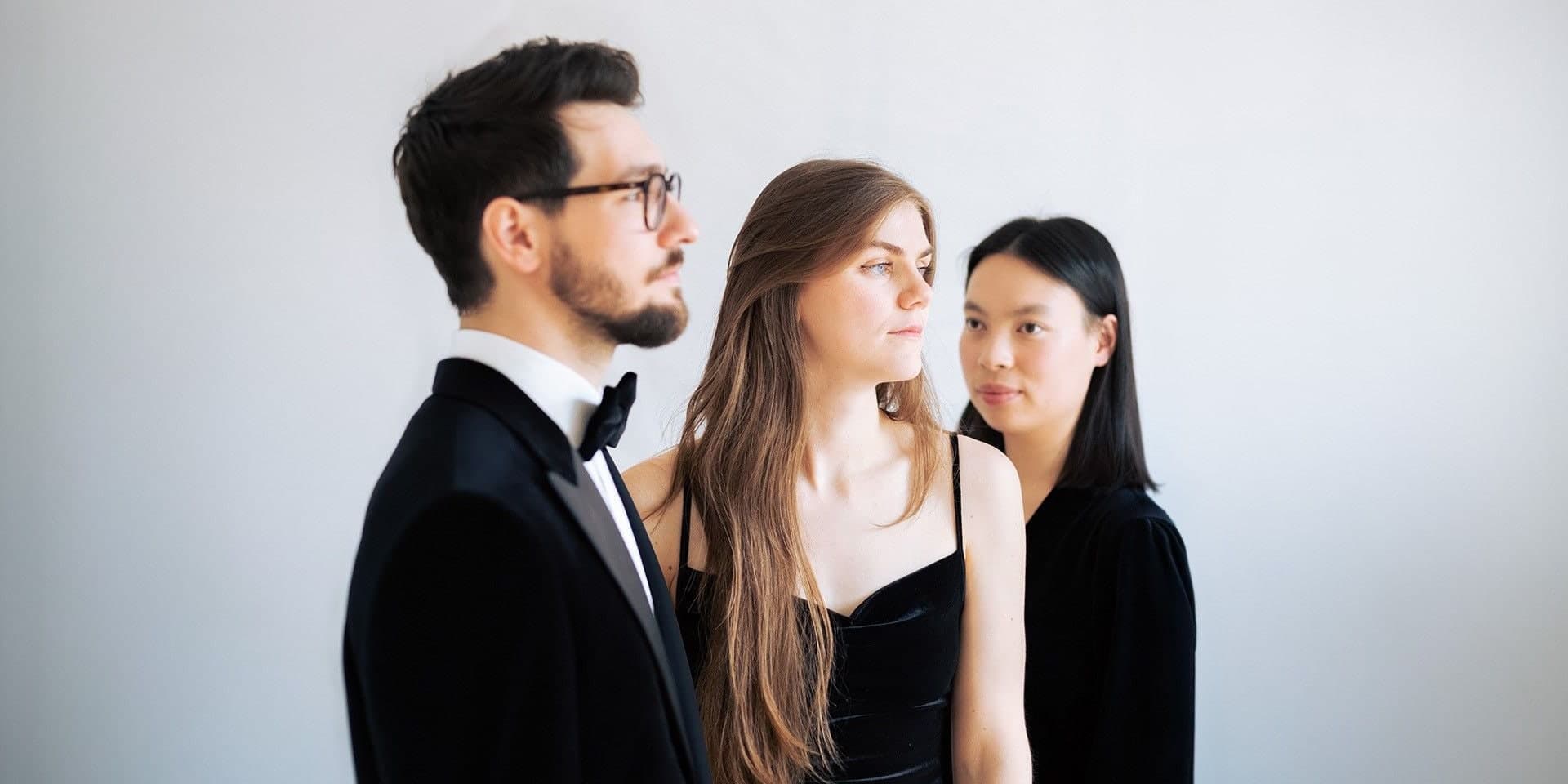 The three members of Trio JAM standing one behind another against a plain wall.