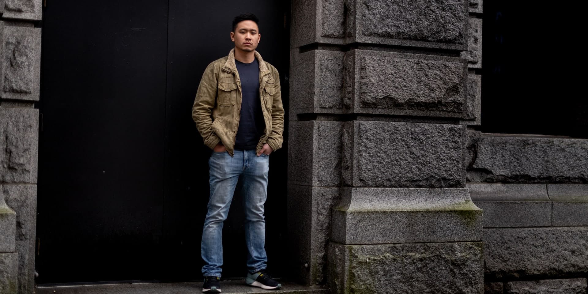 Andrew J. Yang stendur í dyragætt við vegg úr höggnum steini með hendur í vösum.