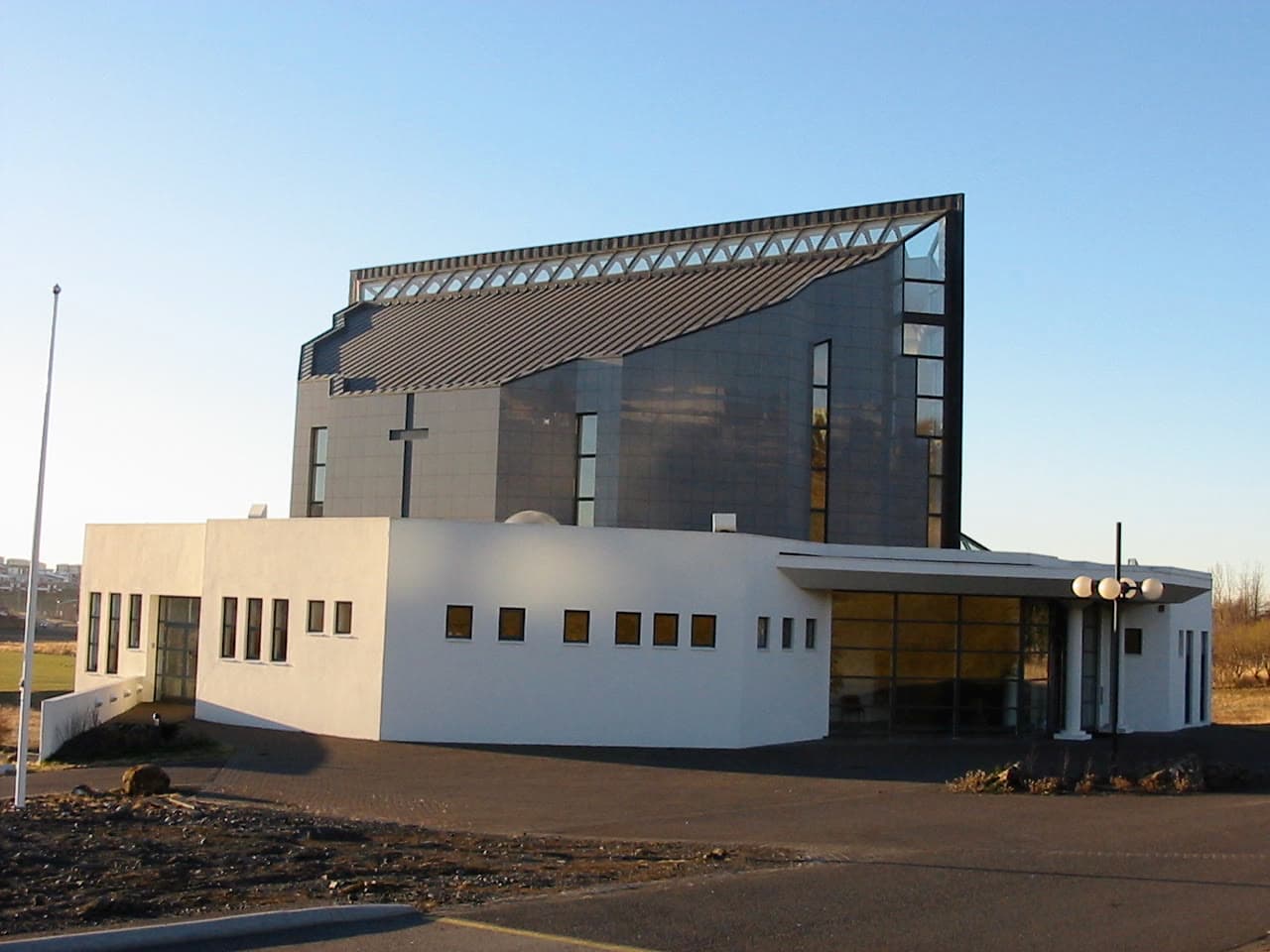 Digraneskirkja, bogadregið þak kirkjuskipsins yfir lágum þjónustubyggingum og kross á gaflinum.