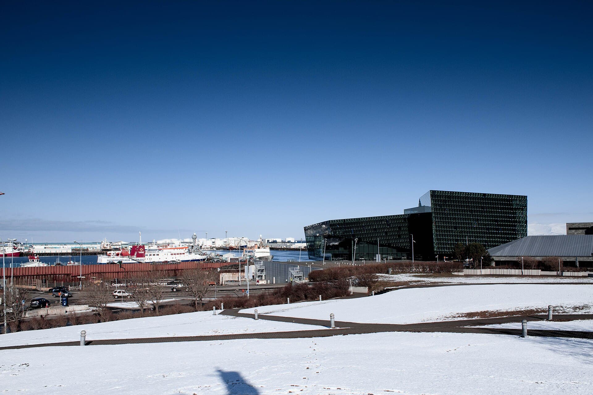 Harpa seen across a snow-covered Arnarhóll, with the harbour behind it.