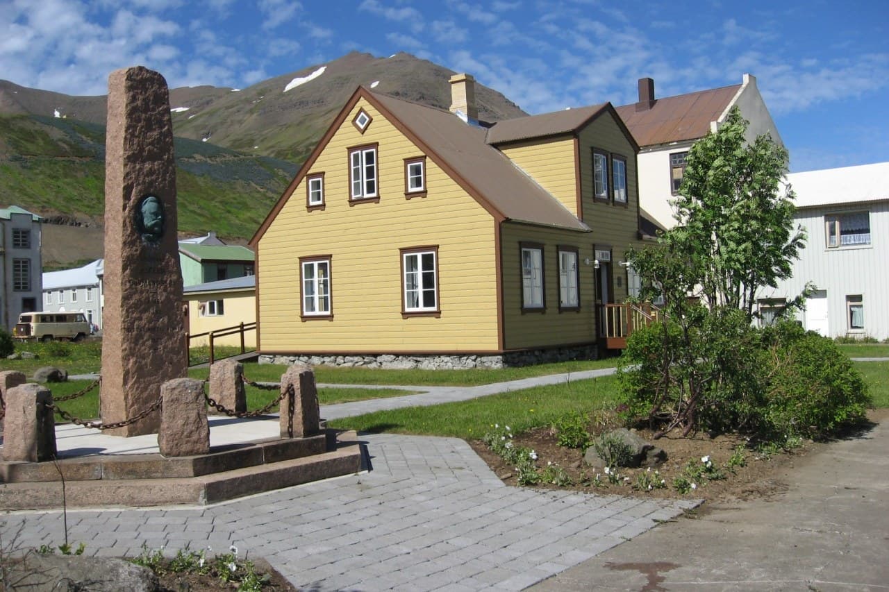Maðdömuhús á Siglufirði, tvílyft timburhús með bröttu þaki, og minnisvarði á stétt framan við það.