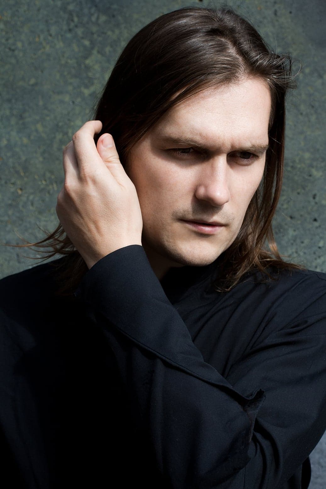 Benedikt Kristjánsson with long hair and a hand at his head, in a black coat.