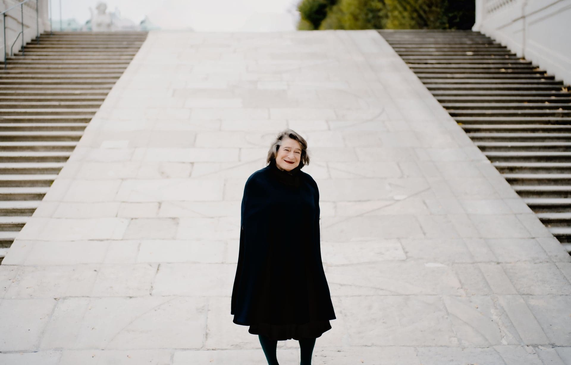 Elisabeth Leonskaja stands in a black coat at the foot of a broad stone staircase.