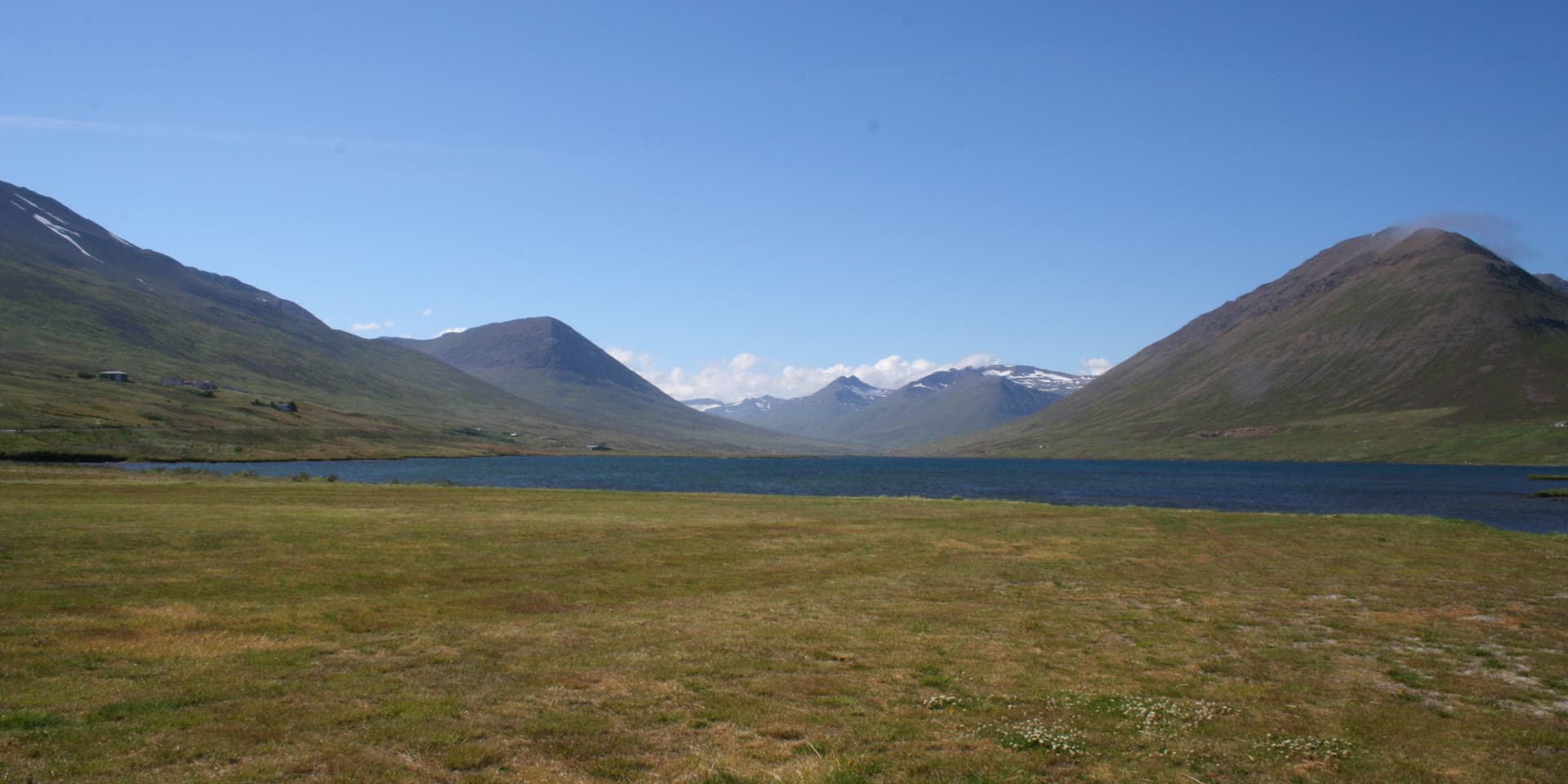 Ólafsfjarðarvatn, the lake at Ólafsfjörður, on a July evening, green mountainsides around it and snow on the peaks beyond.