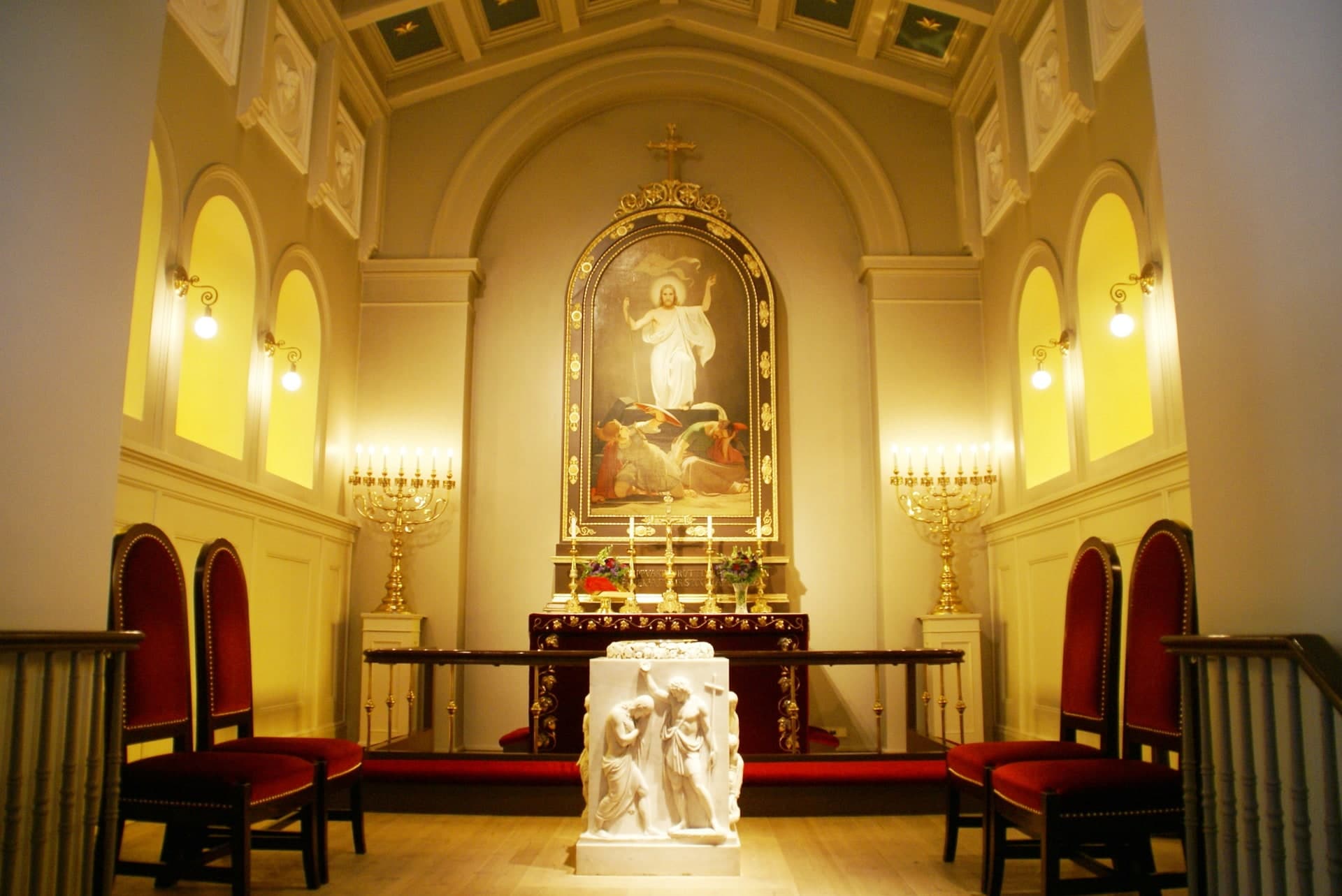 The chancel of Dómkirkjan in warm light, the altarpiece in its arched frame with candlesticks either side and the font in the middle.