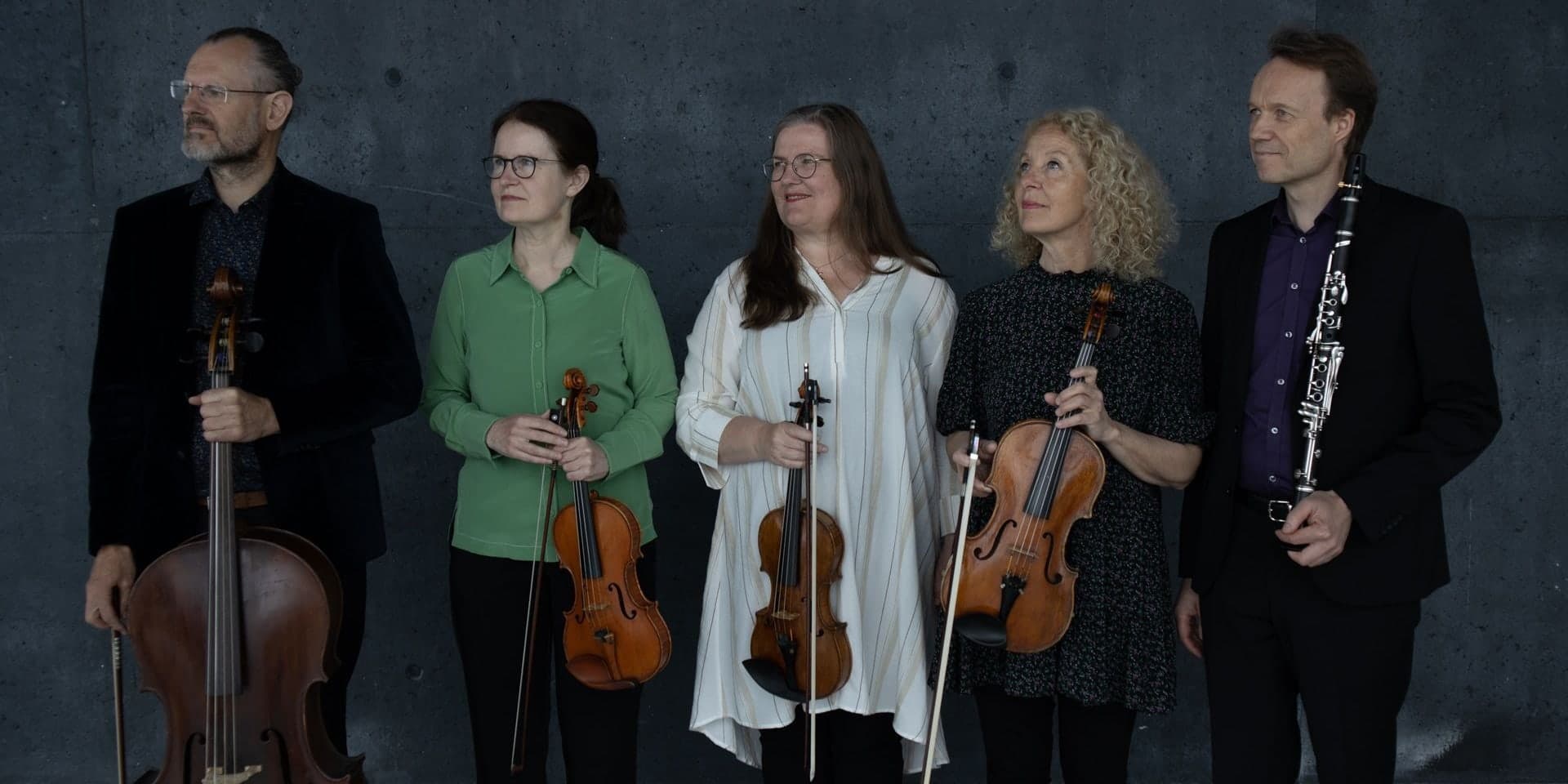 Five of Camerarctica's players standing against a concrete wall with their string instruments and a clarinet.