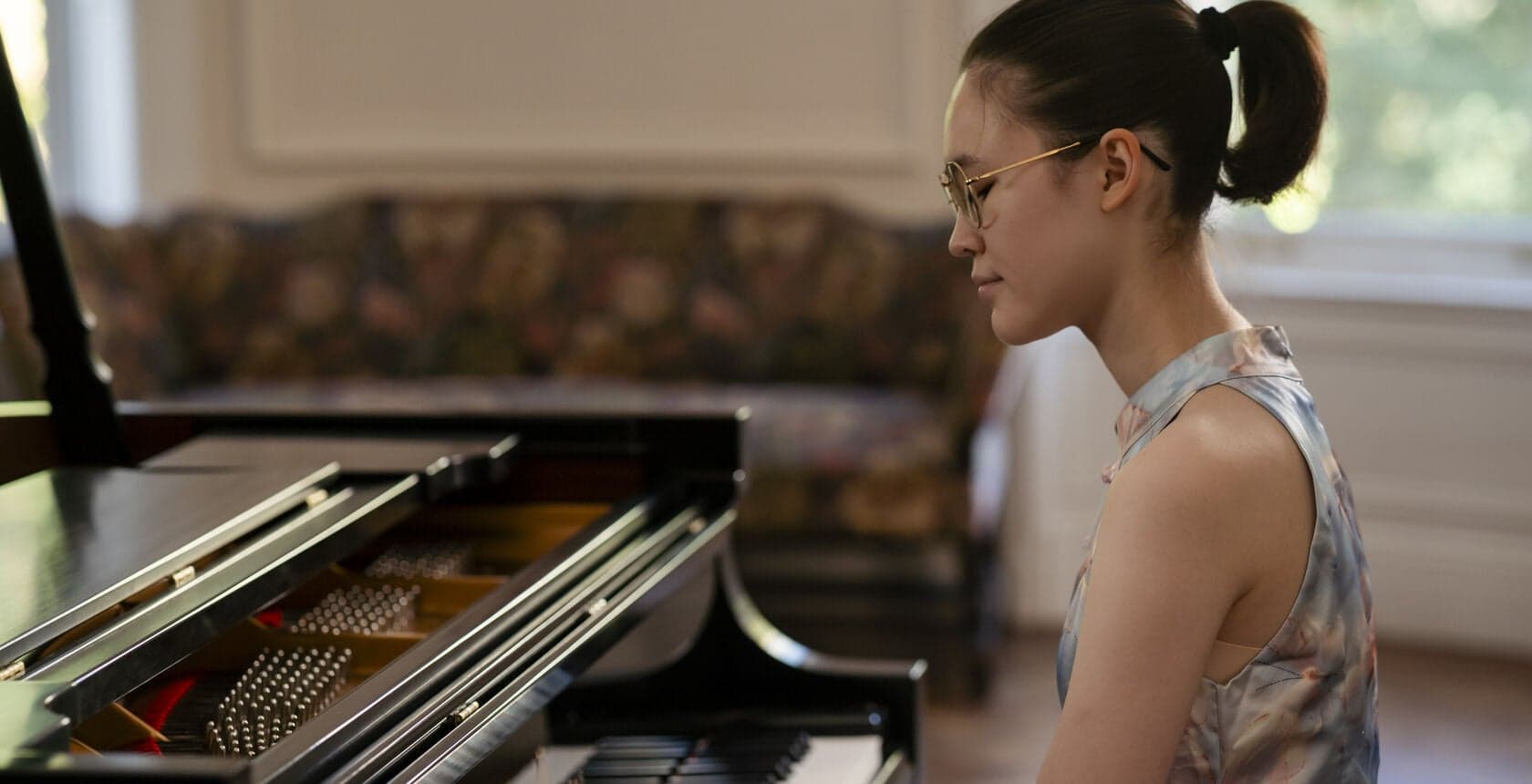 A young woman sits at a grand piano in a bright room.