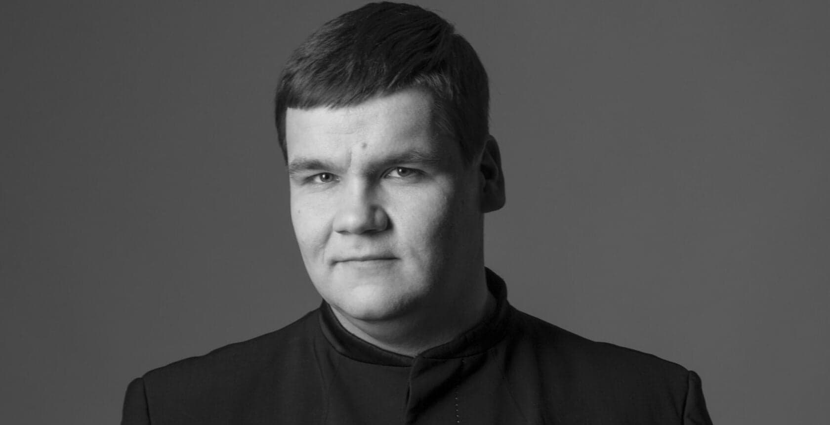 A black-and-white portrait of a man in a dark collarless jacket.
