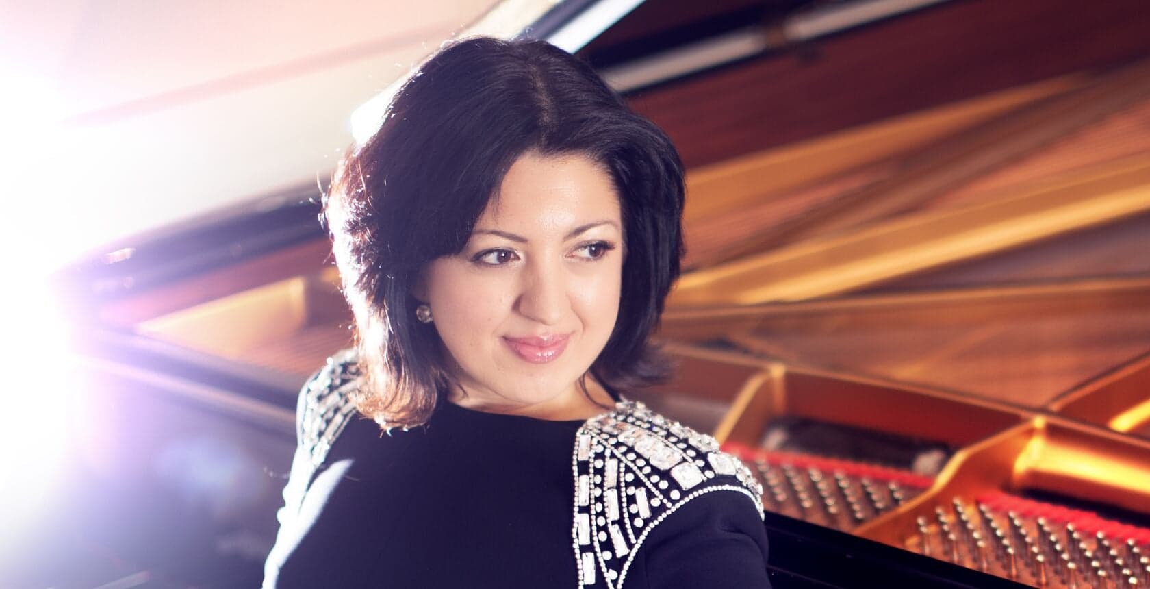 A dark-haired woman beside a grand piano, with streaks of light across the frame.