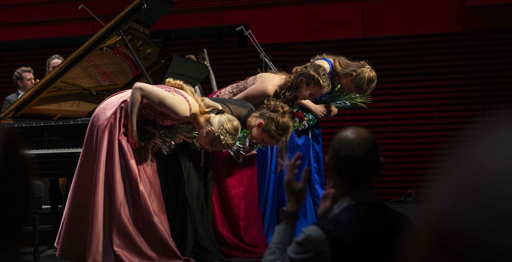A woman in costume lies back across a grand piano, draped in red and blue.