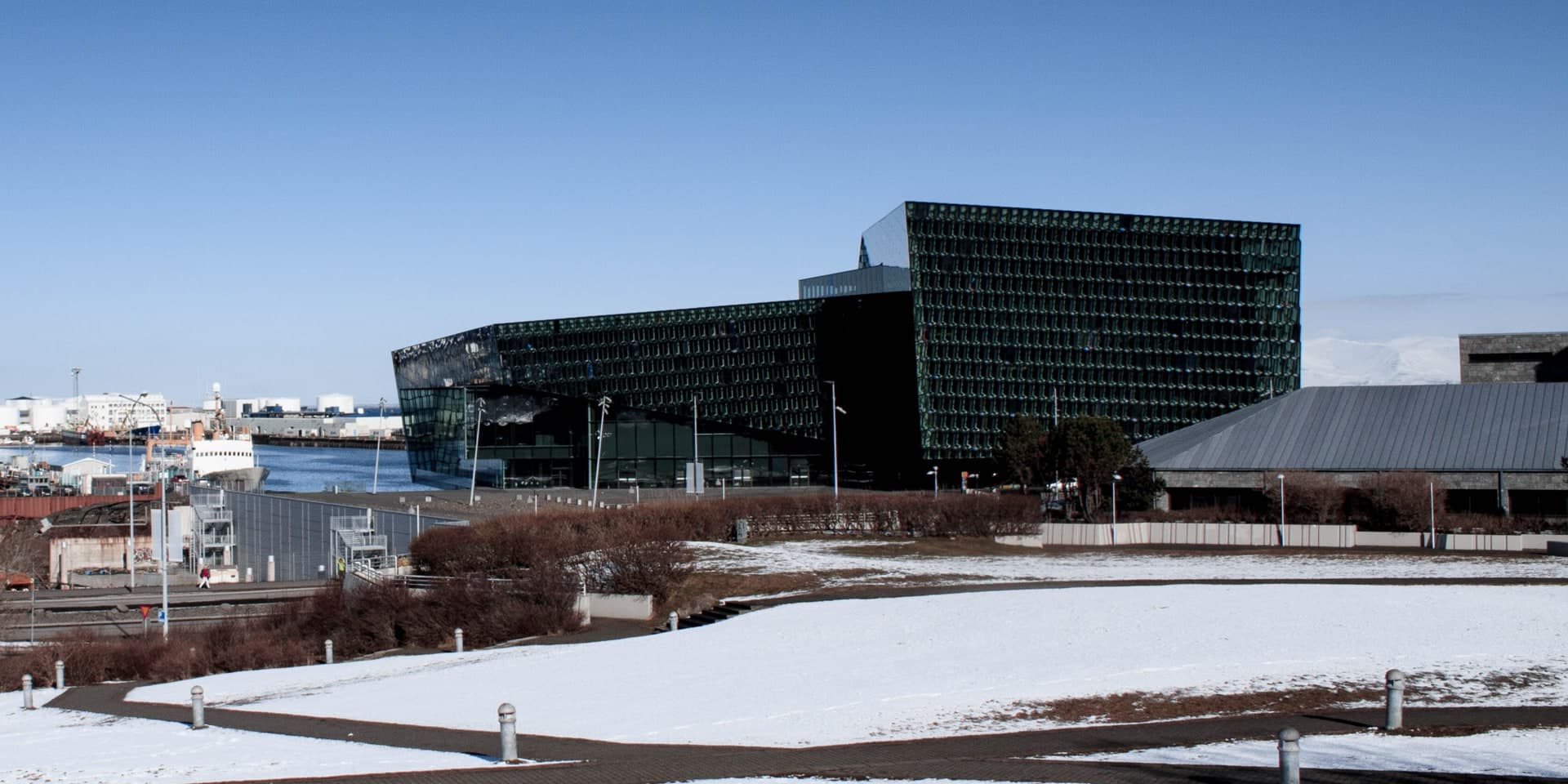 Harpa séð yfir snævi þakinn Arnarhól, glerhjúpurinn snýr að höfninni og fjöllin rísa að baki.