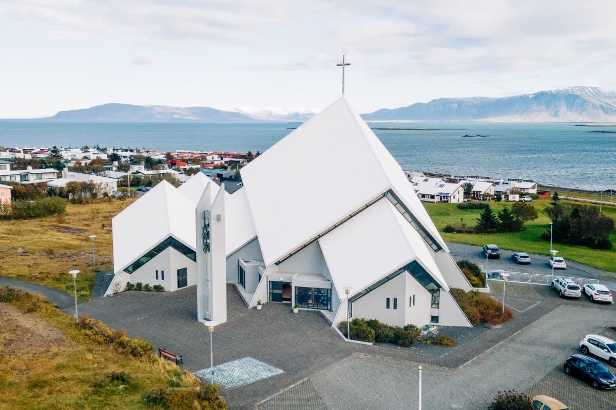 Seltjarnarneskirkja from the air, steep roof planes with a cross rising from them, the town around it and the sea behind.