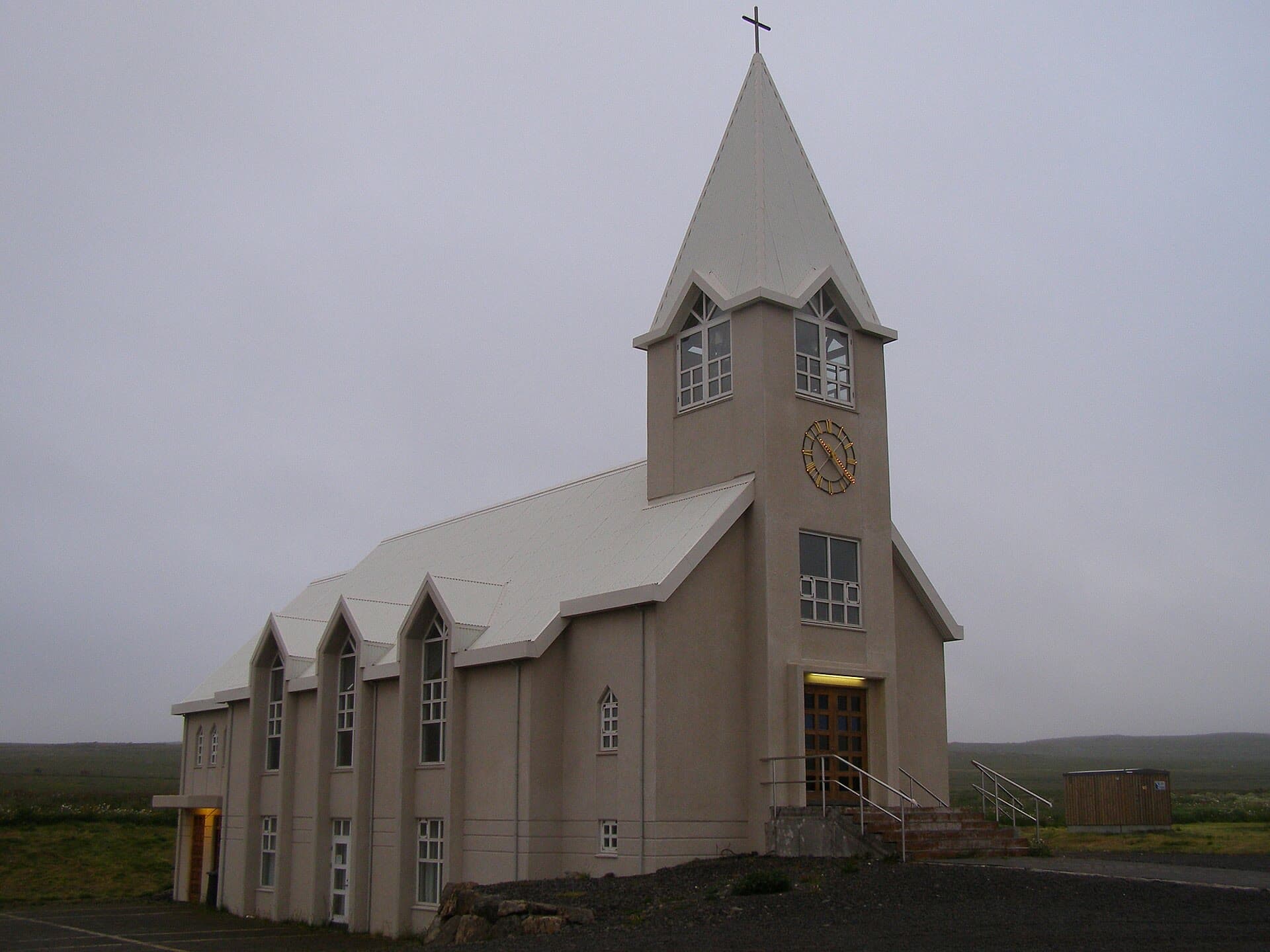 Þórshafnarkirkja framan frá, turn með oddmjóum spíri yfir innganginum og oddbogagluggar niður hliðina.